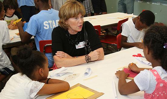 employee sitting at a table talking with 3 children who are doing drawings